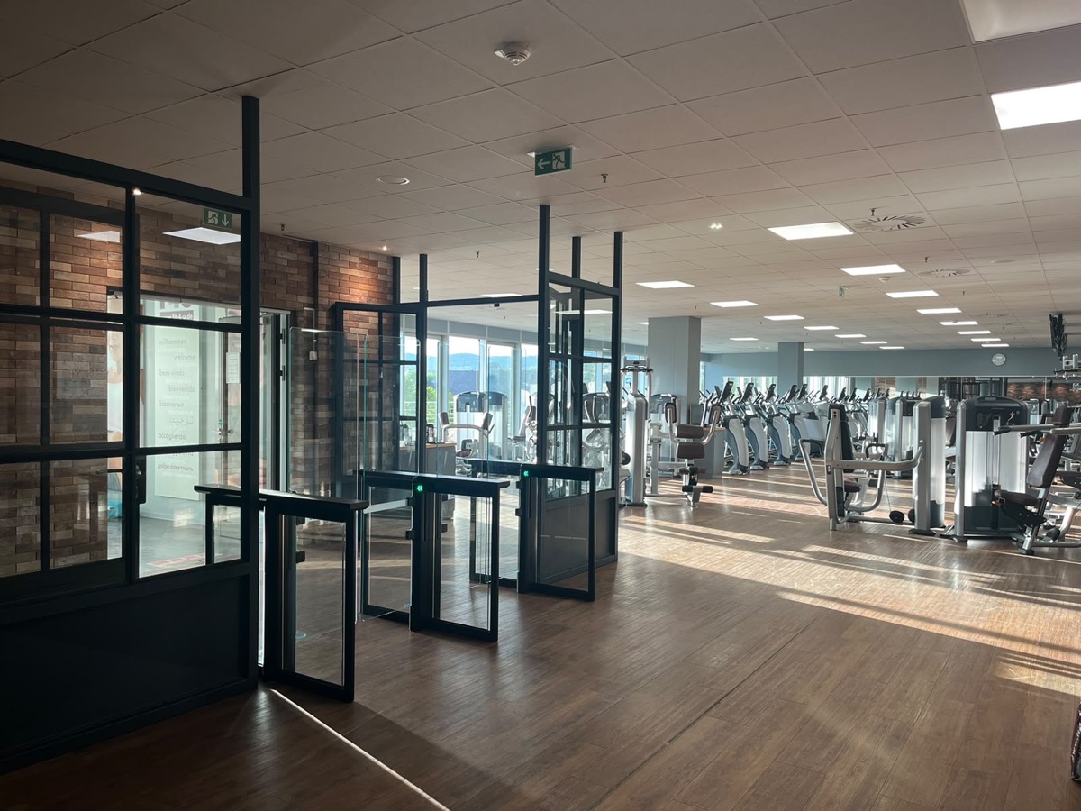 Eingangsbereich des F4U Wiesbaden mit Drehkreuzen und Glastüren vor einer Backsteinwand, dahinter die Cardio- und Kraftfläche an der Fensterfront