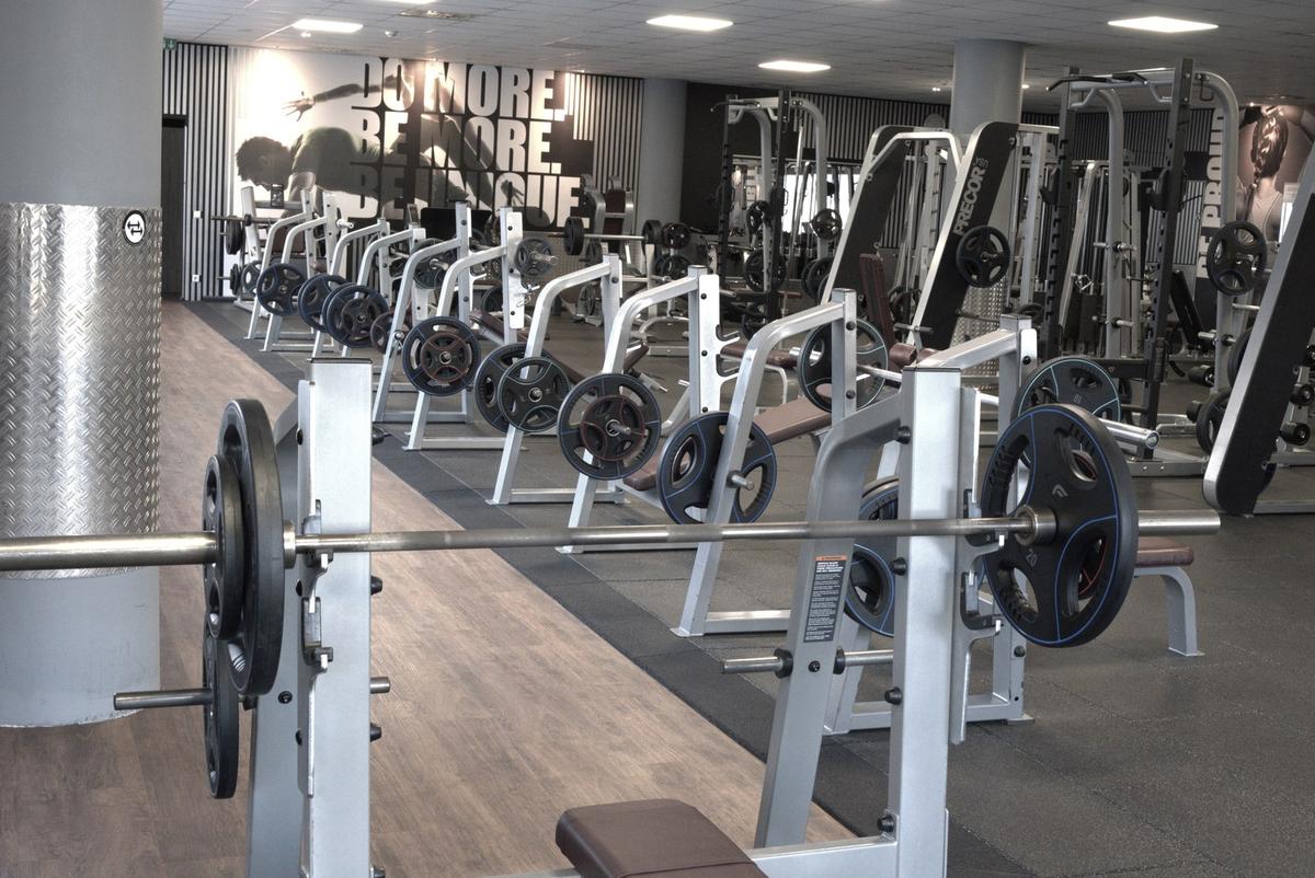Langhantel und Racks im Freihantelbereich des F4U Wiesbaden vor dem Wandbild DO MORE. BE MORE. BE UNIQUE.