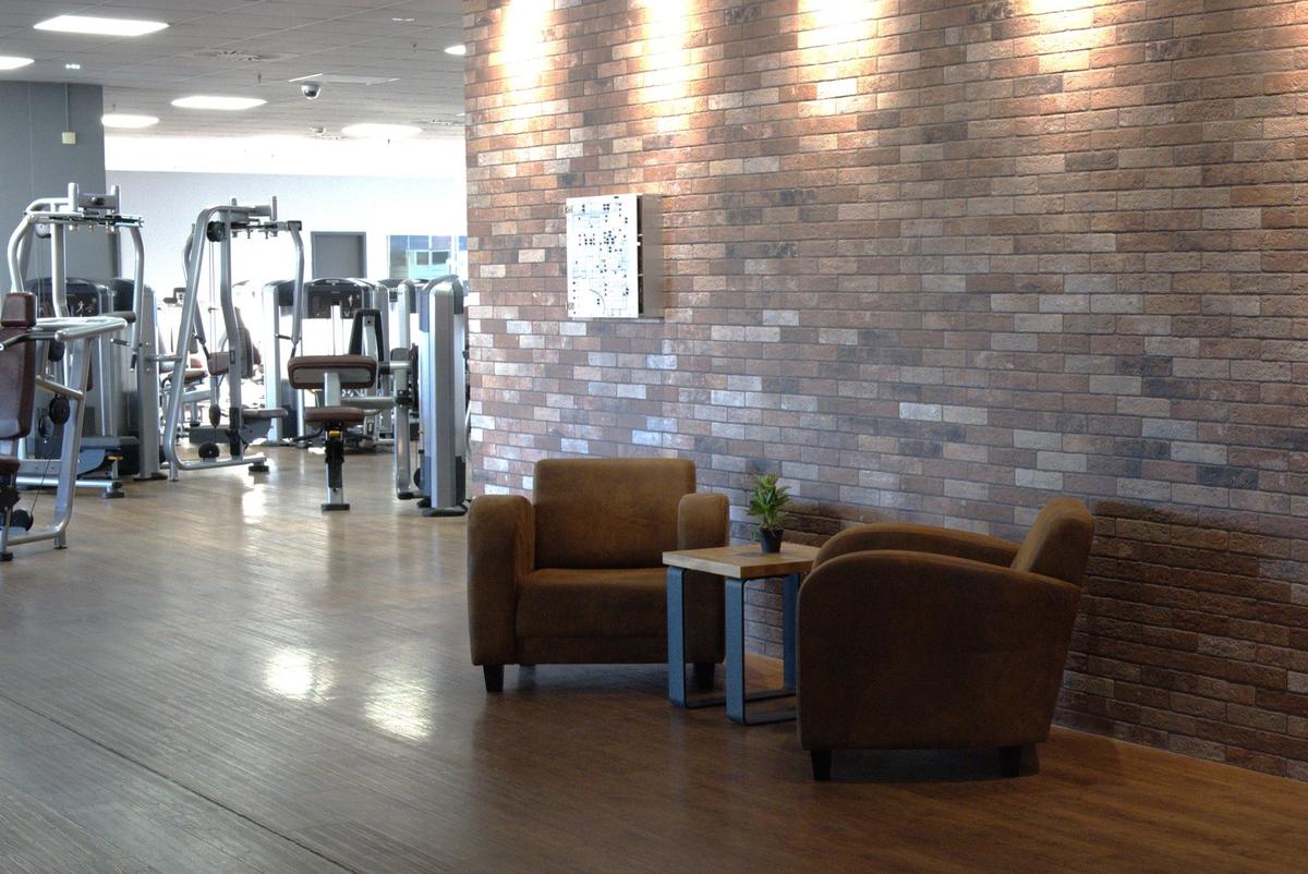 Zwei Sessel mit Beistelltisch vor der Backsteinwand in der Lounge des F4U Wiesbaden, dahinter die Trainingsfläche